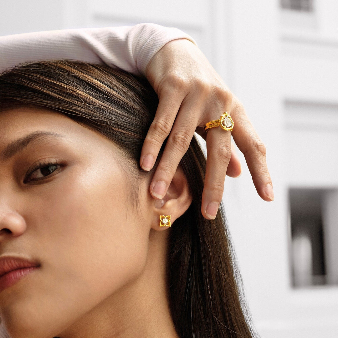 Risis Vintage Bamboo Ring with White Topaz - A person showcases a gold ring and matching earrings with intricate designs; the jewelry glistens, highlighting its craftsmanship and elegance.