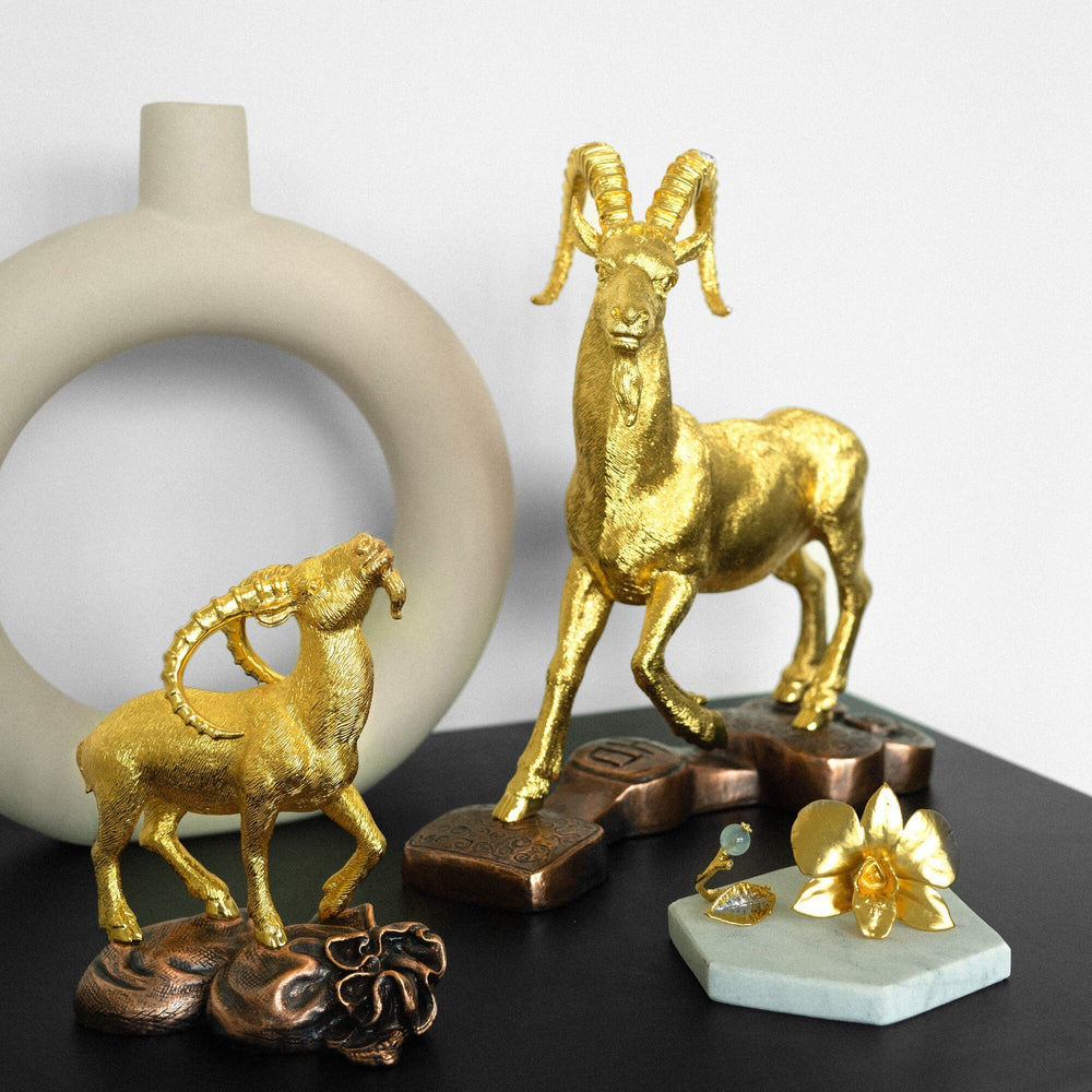 Risis Wealth Goat - Golden sculptures of a majestic ibex with large curved horns and a horse with spiraled features stand elegantly, surrounded by ornate bronzed pieces and a delicate golden orchid.